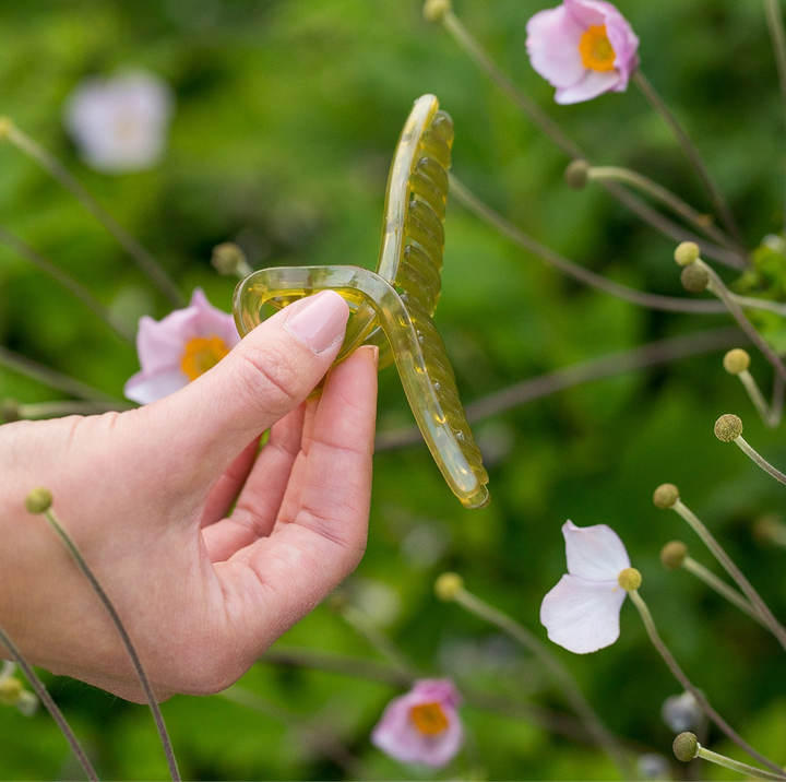 Sage Green Claw Clip held against pink flowers, showing its soft translucent finish