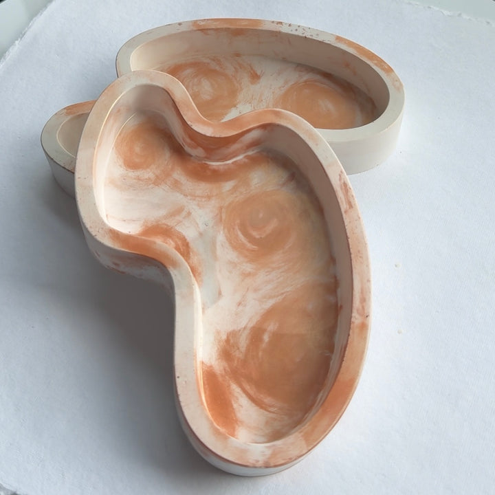 Handmade wavy resin jewelry tray with a marbled finish displayed on a vanity, holding rings and earrings.