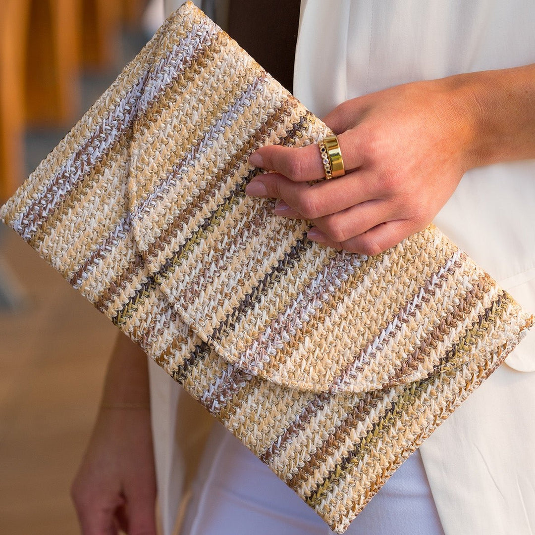 Woven straw clutch bag with tan, cream, brown, and white stripes, featuring a secure flap closure.