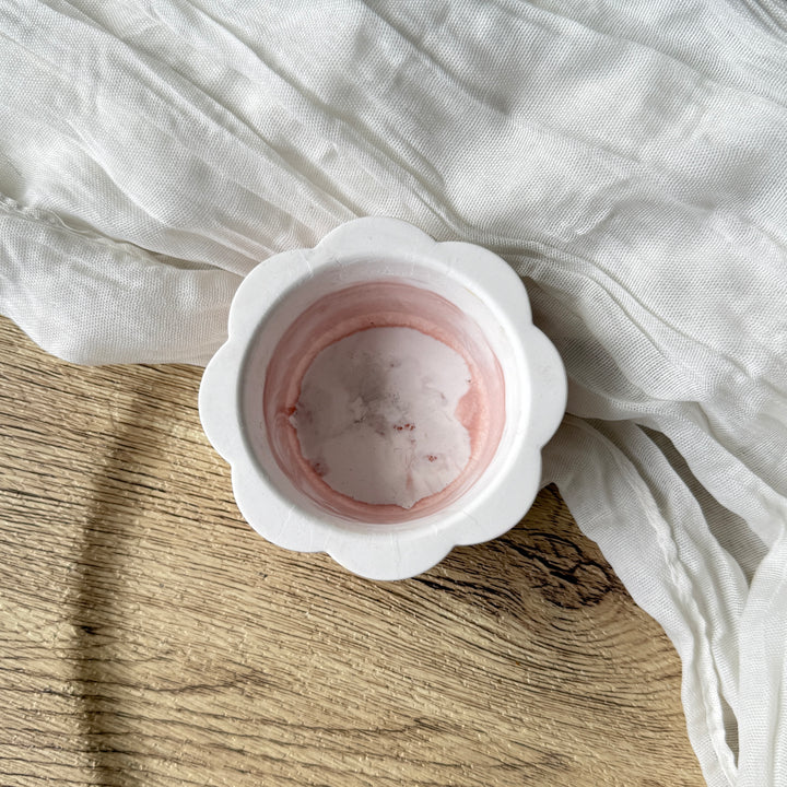 White ceramic bowl with pink interior on a wooden surface with white fabric
