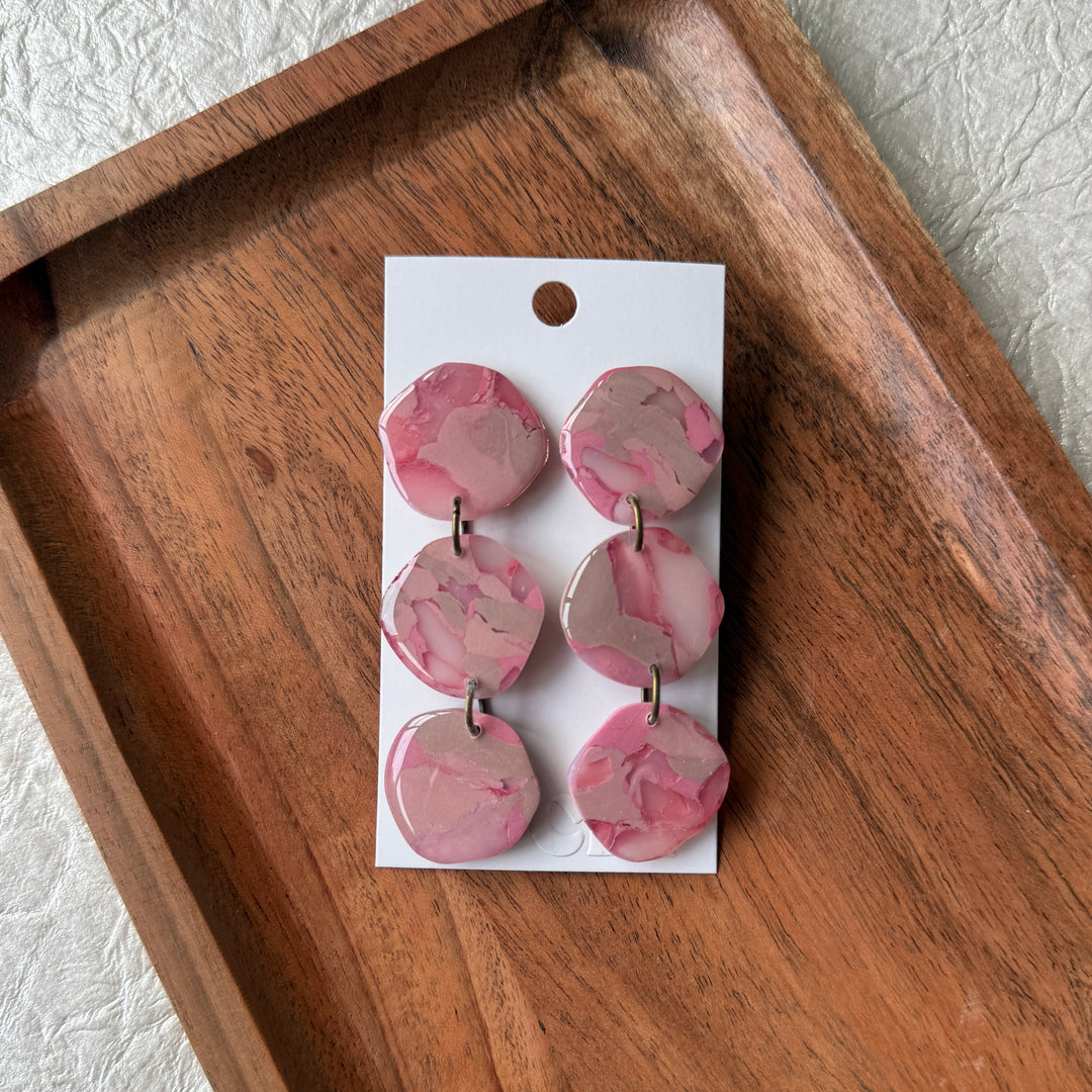 Pink marbled earrings on a white card with a wooden tray below