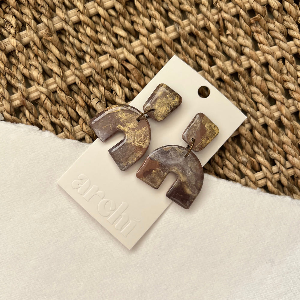 Neutral-toned handmade arched statement earrings in brown, tan, and gold on Archi earring card with woven texture