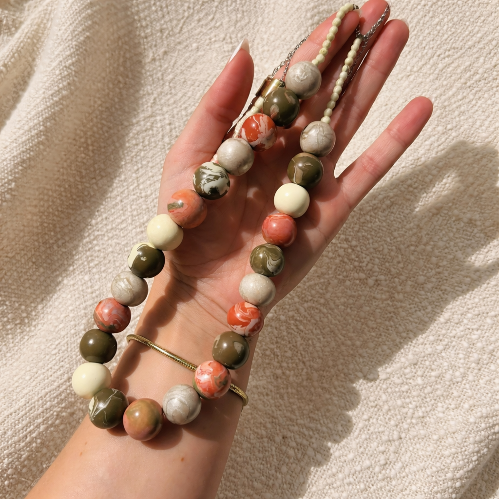 Hand holding a beaded necklace with various colored beads on a beige background
