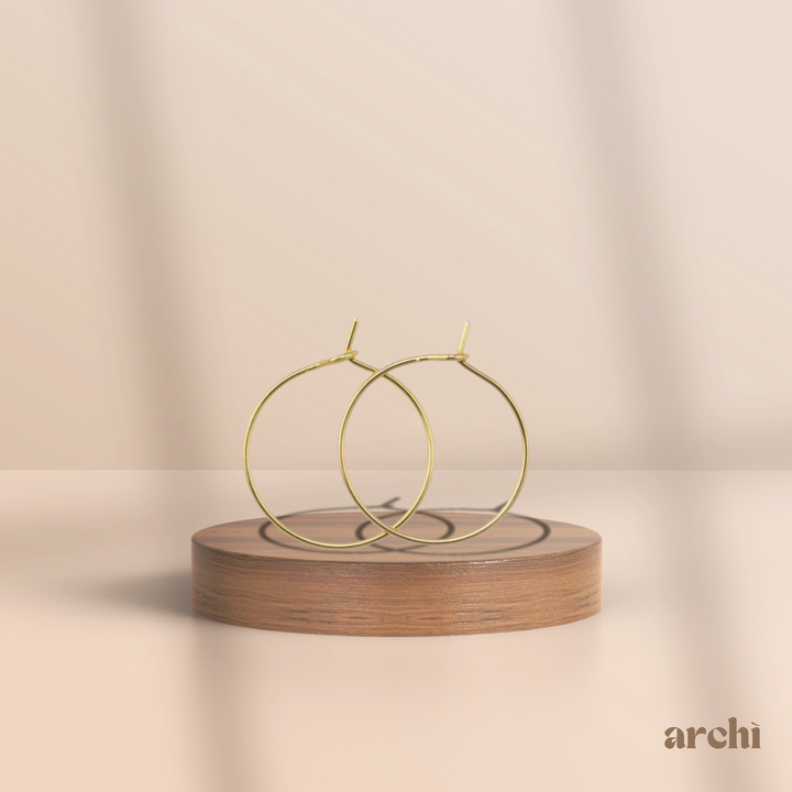 Isla Gold Hoop Earrings displayed on a wooden stand, featuring a minimalist 14K gold-plated design.